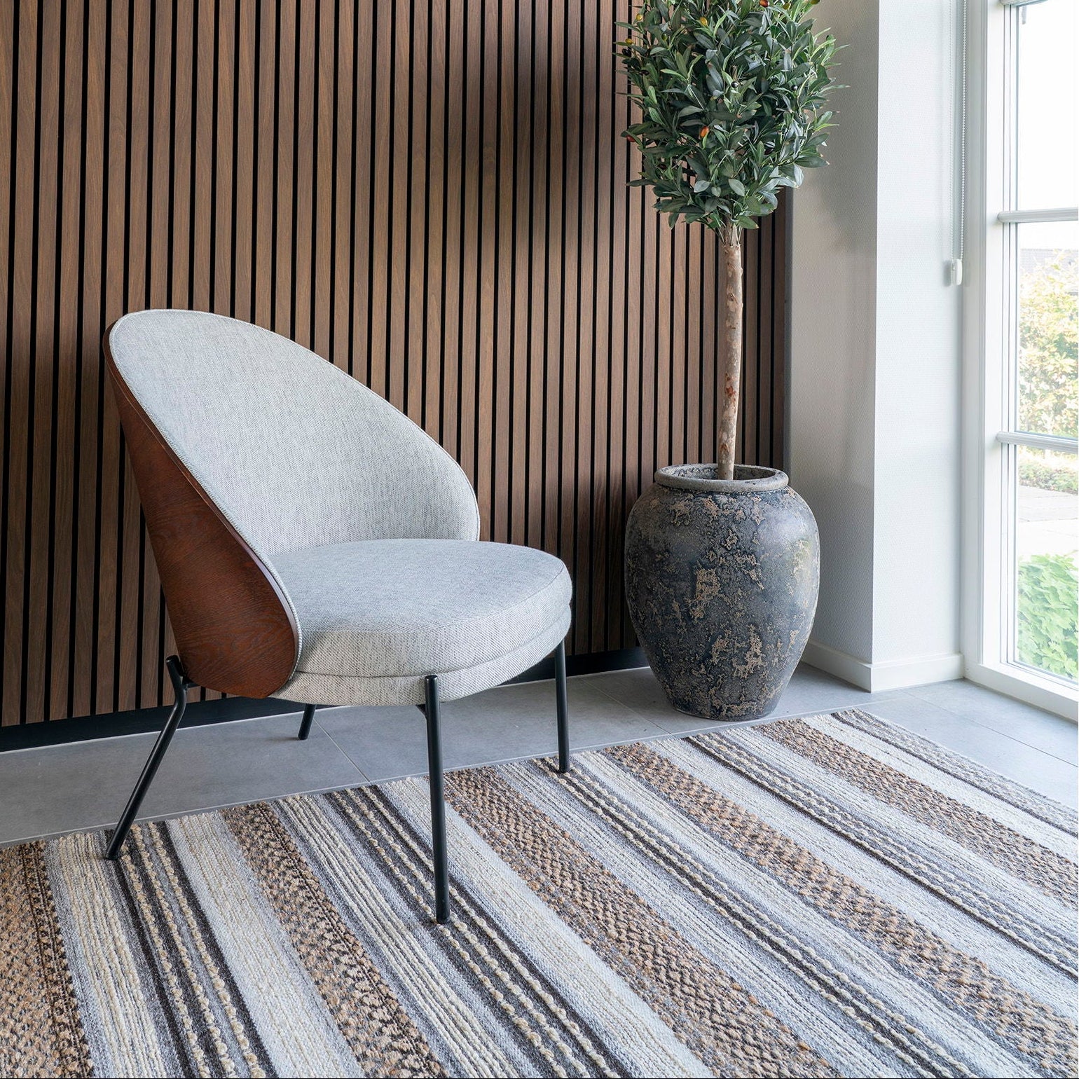 Modern chair against a slatted wood wall with a plant and striped rug.